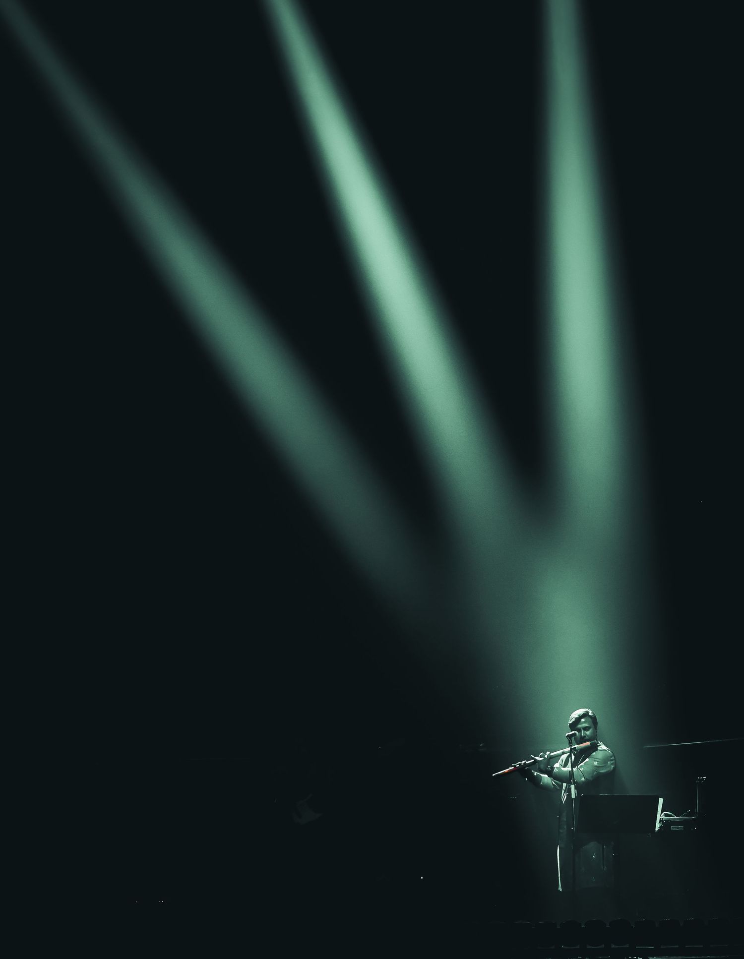 Artistic black and white photograph of an artist playing flute against a blurred dark background with soft green highlights.