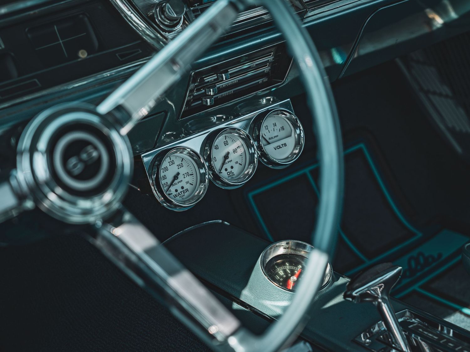 Close-up view of vintage car dashboard showing classic analog gauges and chrome details in dark lighting.