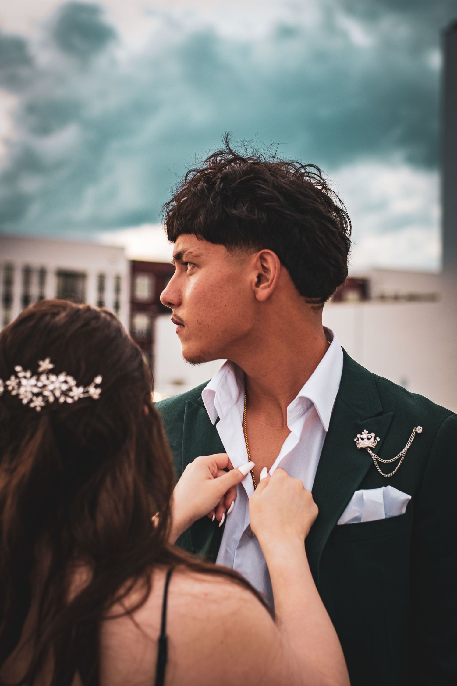 Romantic couple in formal attire embracing outdoors under moody teal-tinted skies.
