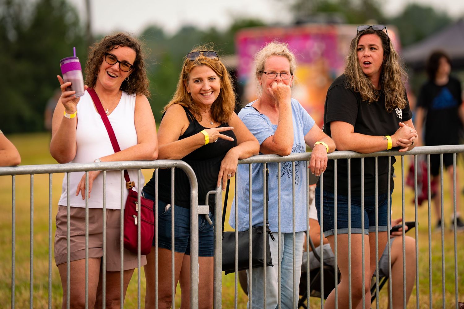 Festival attendees lean against a metal barrier at an outdoor event on a summer day.
