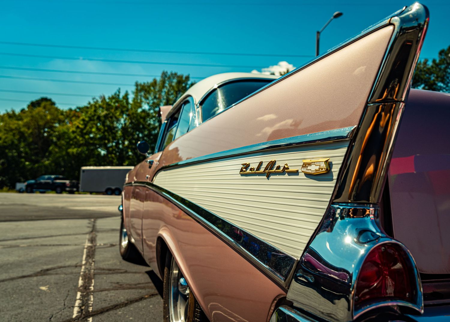 Classic vintage car with chrome trim and reflective paint glimmers under bright sunlight in a parking lot.