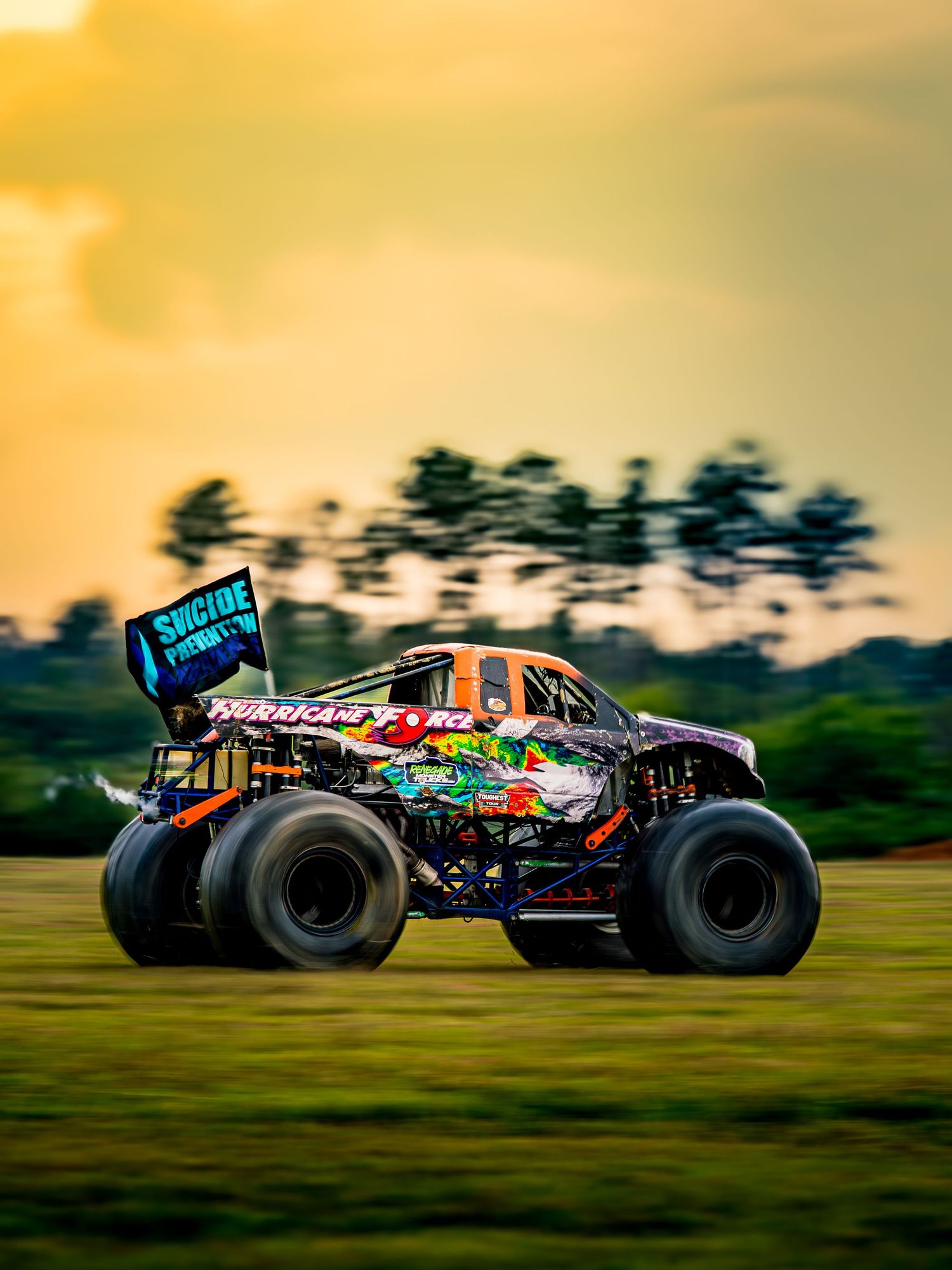 Colorfully decorated RC monster trucks racing across a grassy field at sunset.