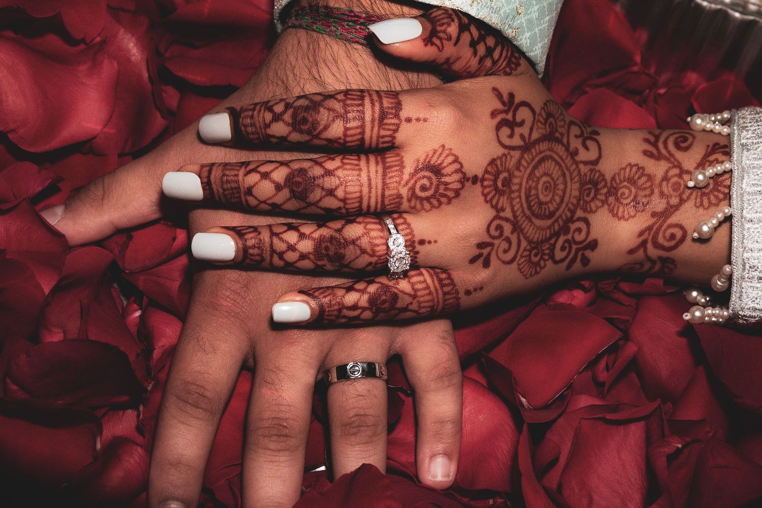 Intricate henna designs displayed on hands with white nail polish against red backdrop.