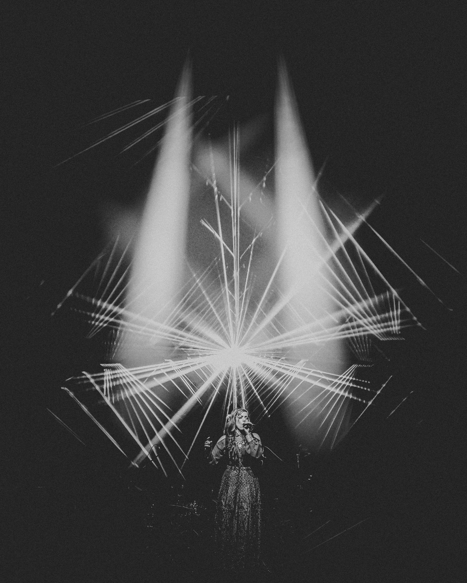 Dramatic black and white concert lighting creates geometric patterns and beams against dark background during performance.