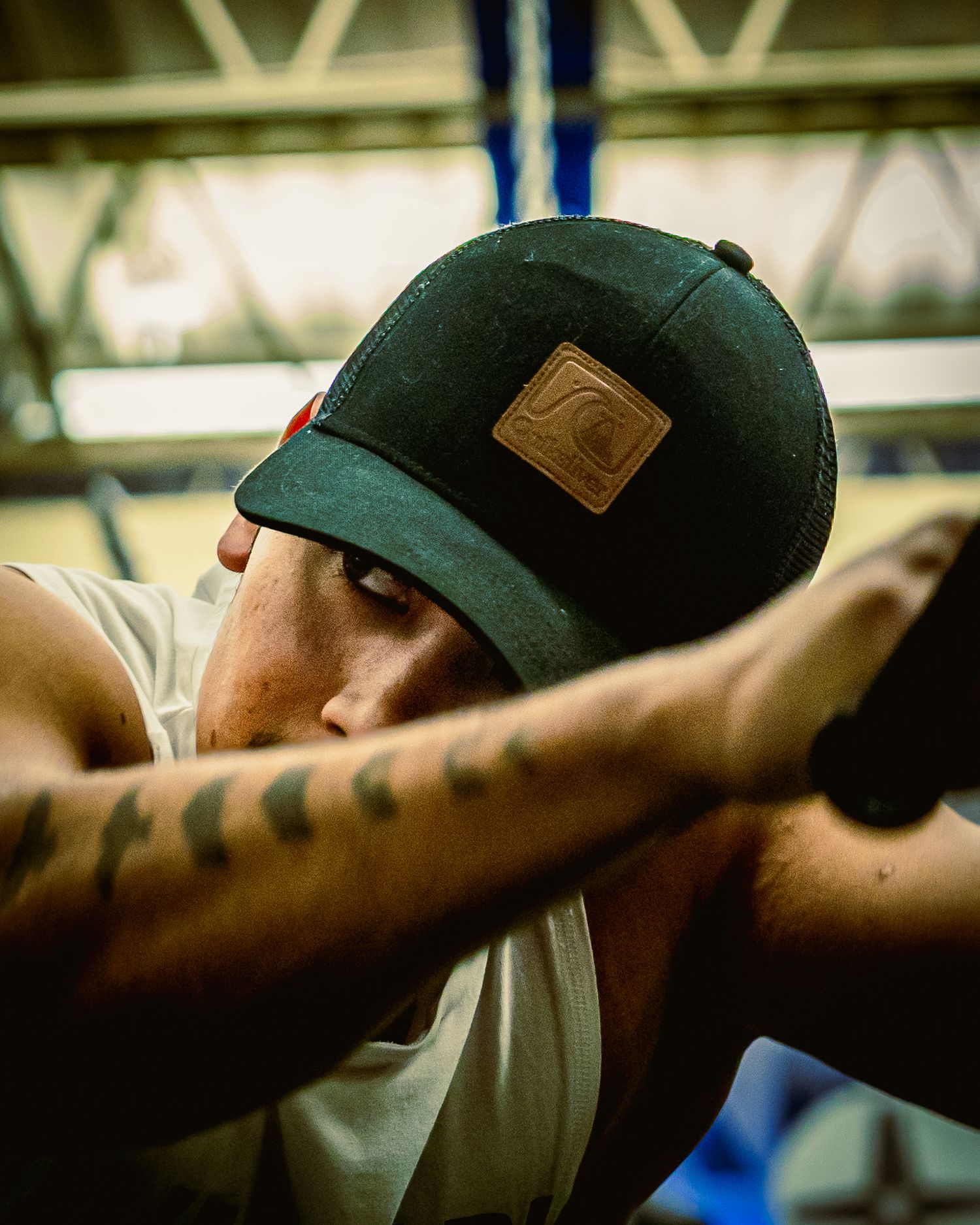 A close-up shot shows someone wearing a dark baseball cap with a leather patch, resting against a tattooed arm.