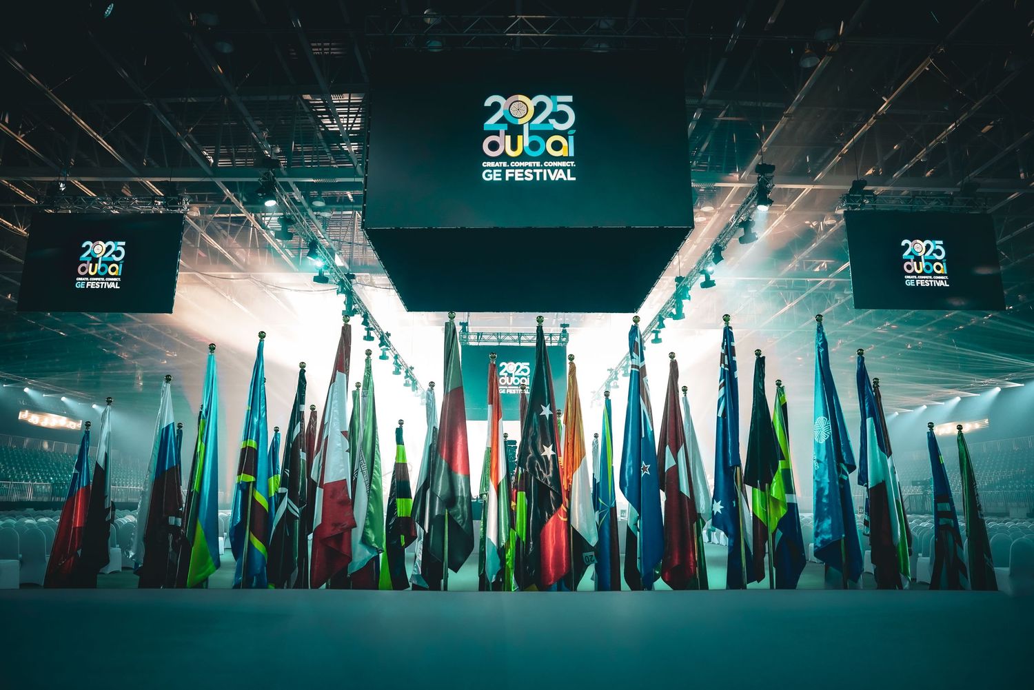 International flags displayed at a Global Festival in Dubai venue with glowing turquoise lighting and digital screens mounted overhead.