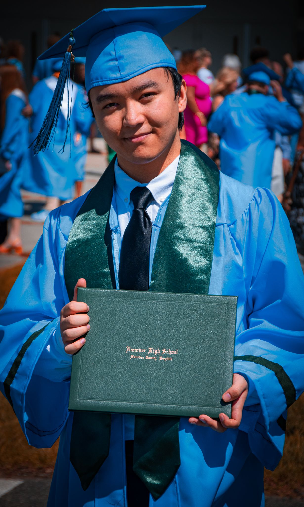 Graduate in blue regalia displays diploma holder with proud smile.