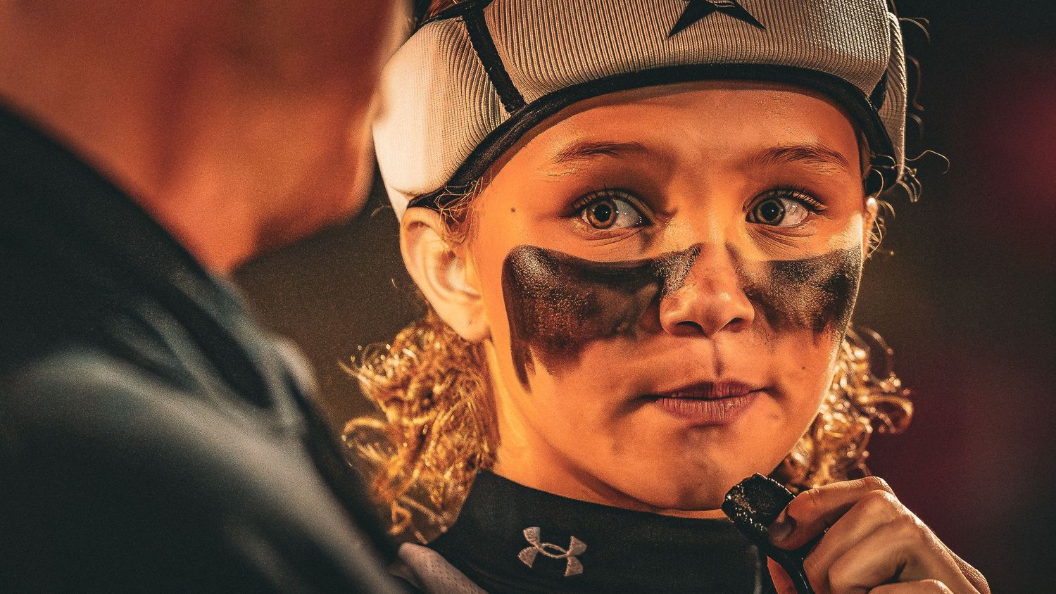 Athlete wearing Under Armour gear and eye black face paint looks focused during nighttime competition.
