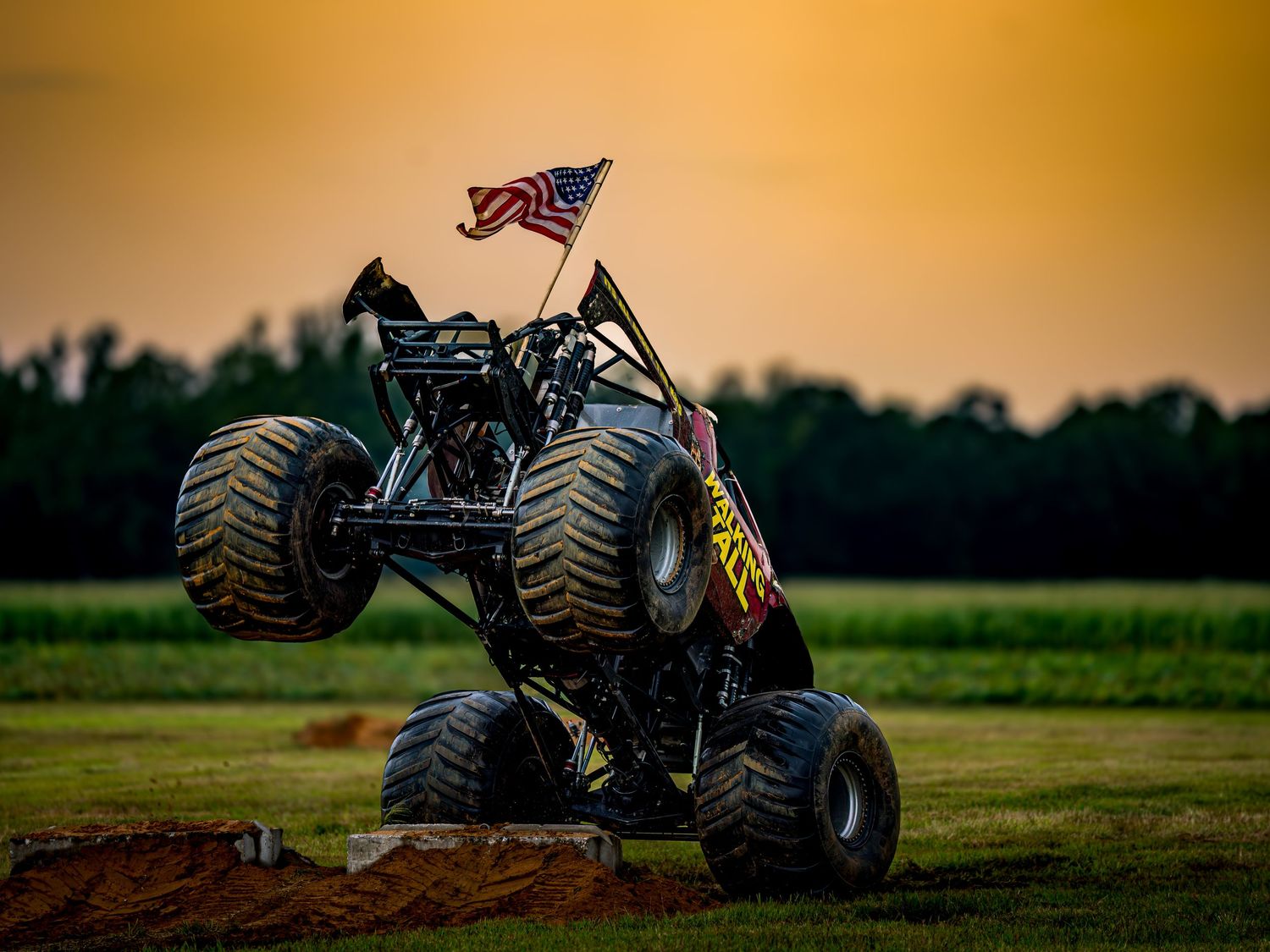 Off-road monster trucks performing stunts on dirt track during sunset competition.