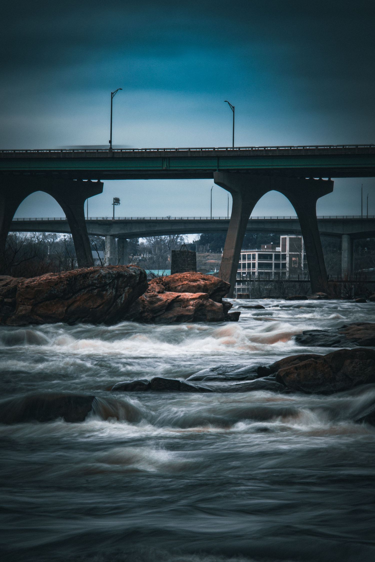 Turbulent waters crash beneath a bridge with dramatic moody lighting and dark blue tones.