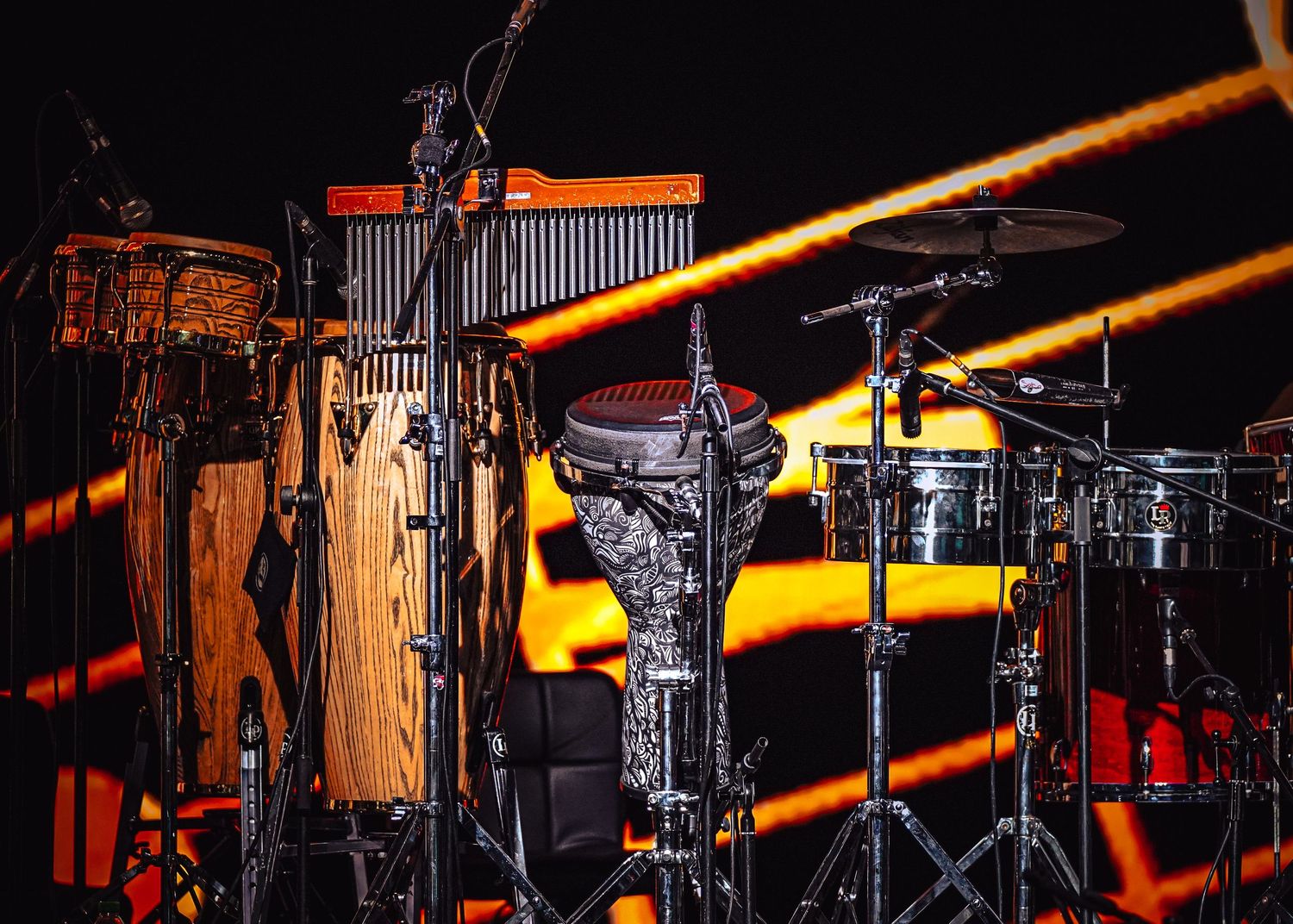 Dramatic concert stage lighting with orange beams illuminating silhouetted musical equipment and instruments.