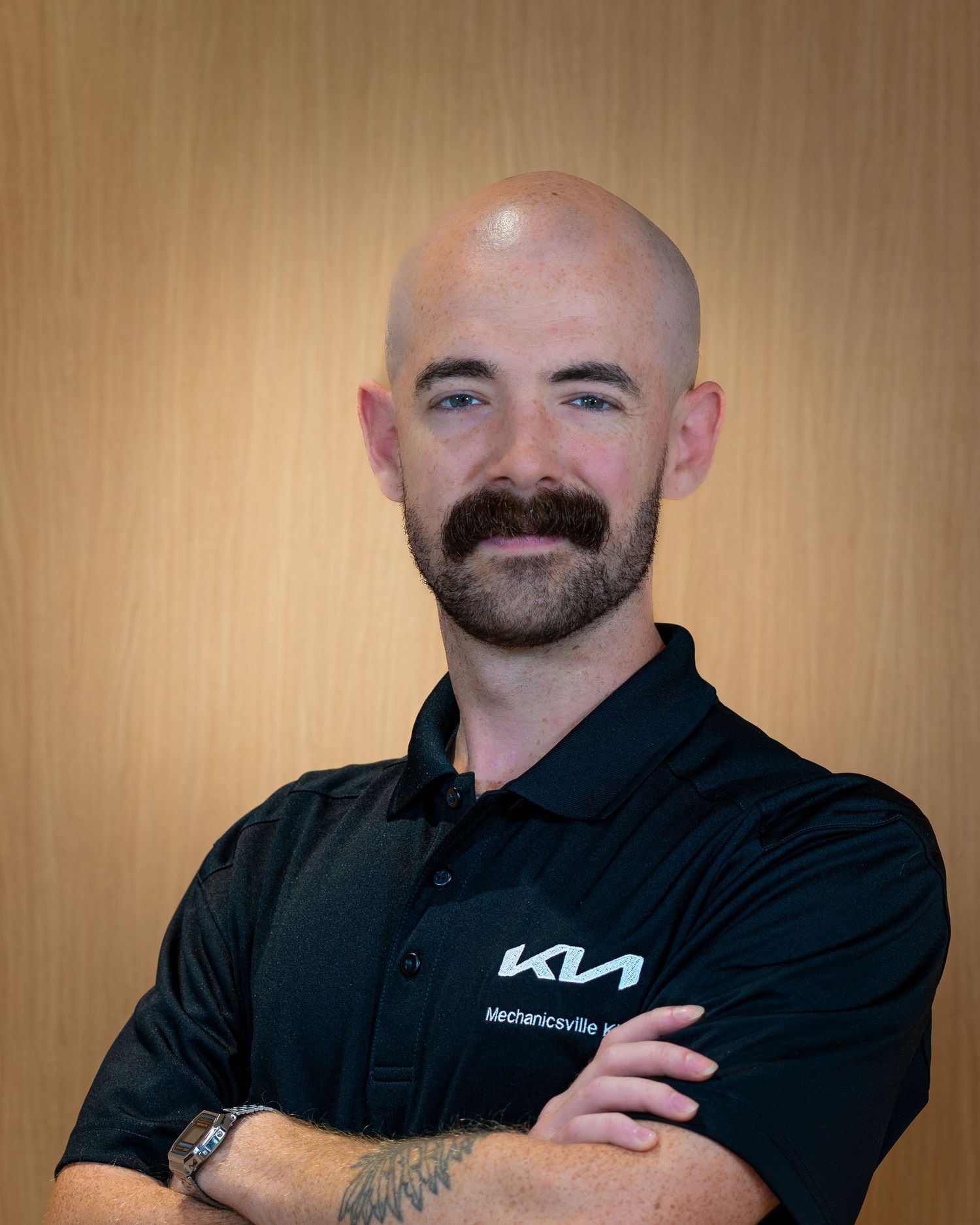 Professional in a black polo shirt with a company logo poses against a warm beige background.
