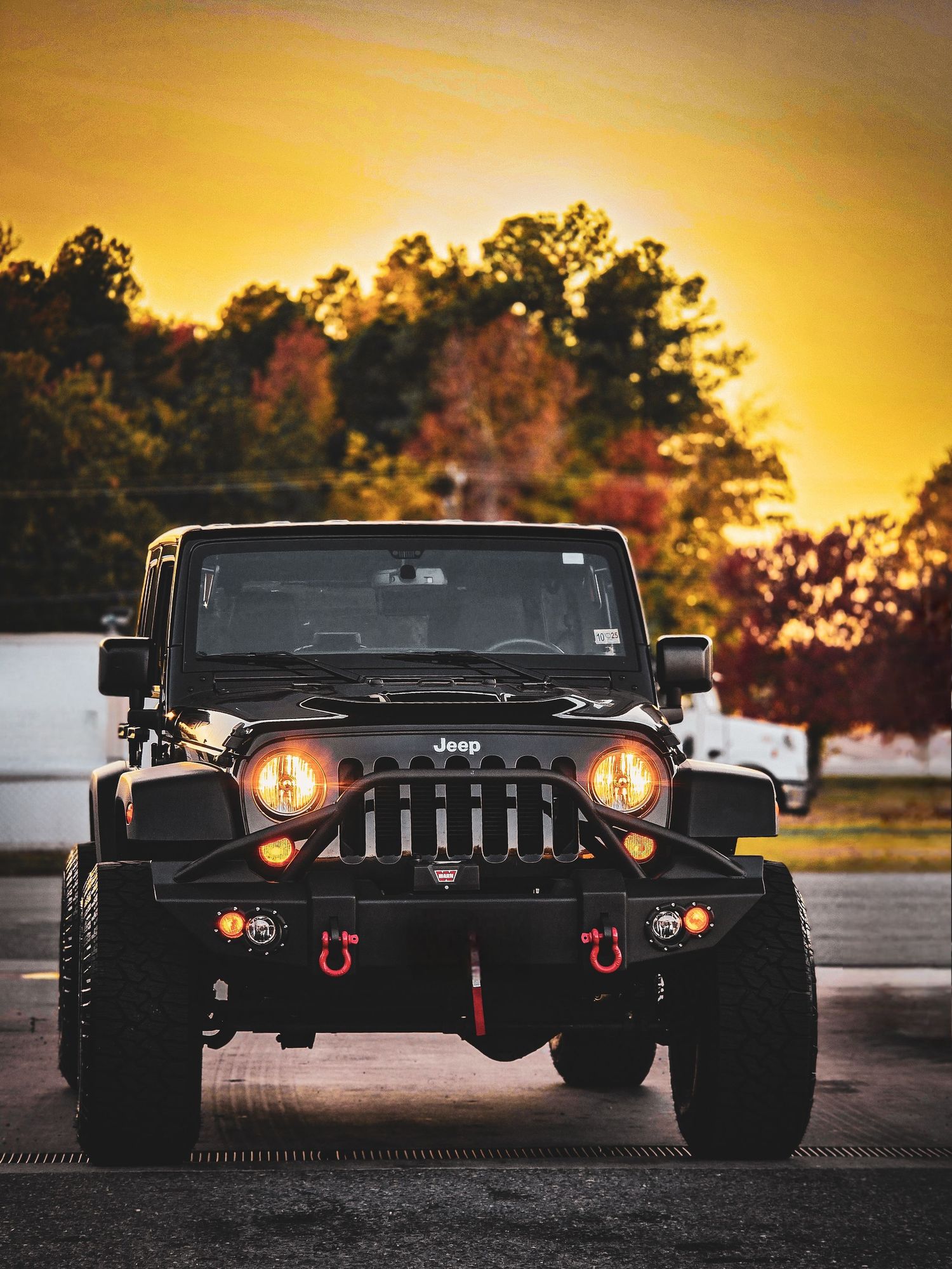 Black Jeep Wrangler front profile silhouetted at sunset showcasing custom headlights and bumper.