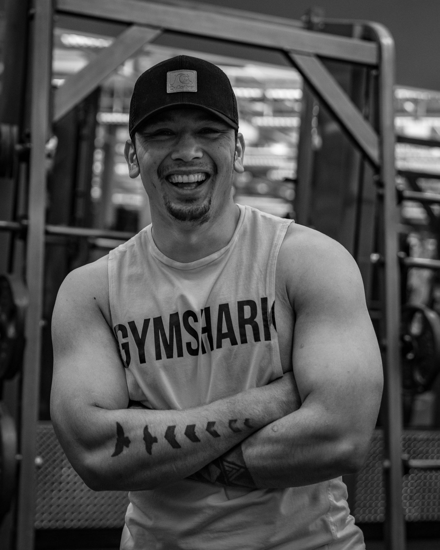 Black and white photo of someone in a Gymshark tank top smiling with crossed arms at the gym.