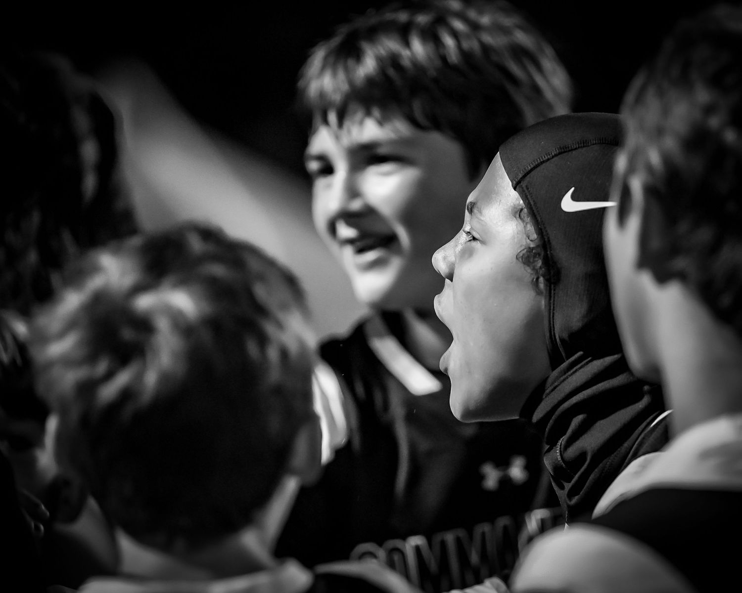 A candid black and white photo shows teammates sharing a joyful moment of laughter together during a sporting event.