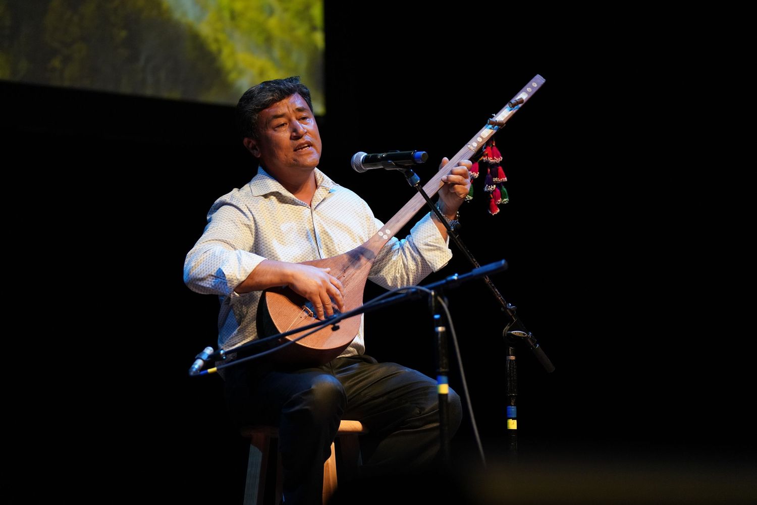 Musicians performing on stage with acoustic instruments against a dark background.