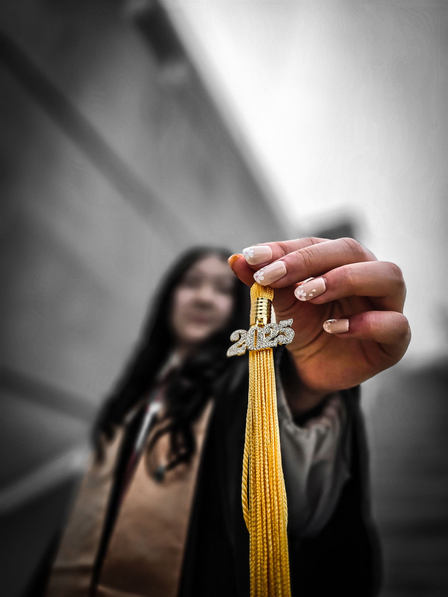 Close-up of graduation tassel being held up with selective color highlighting the gold.