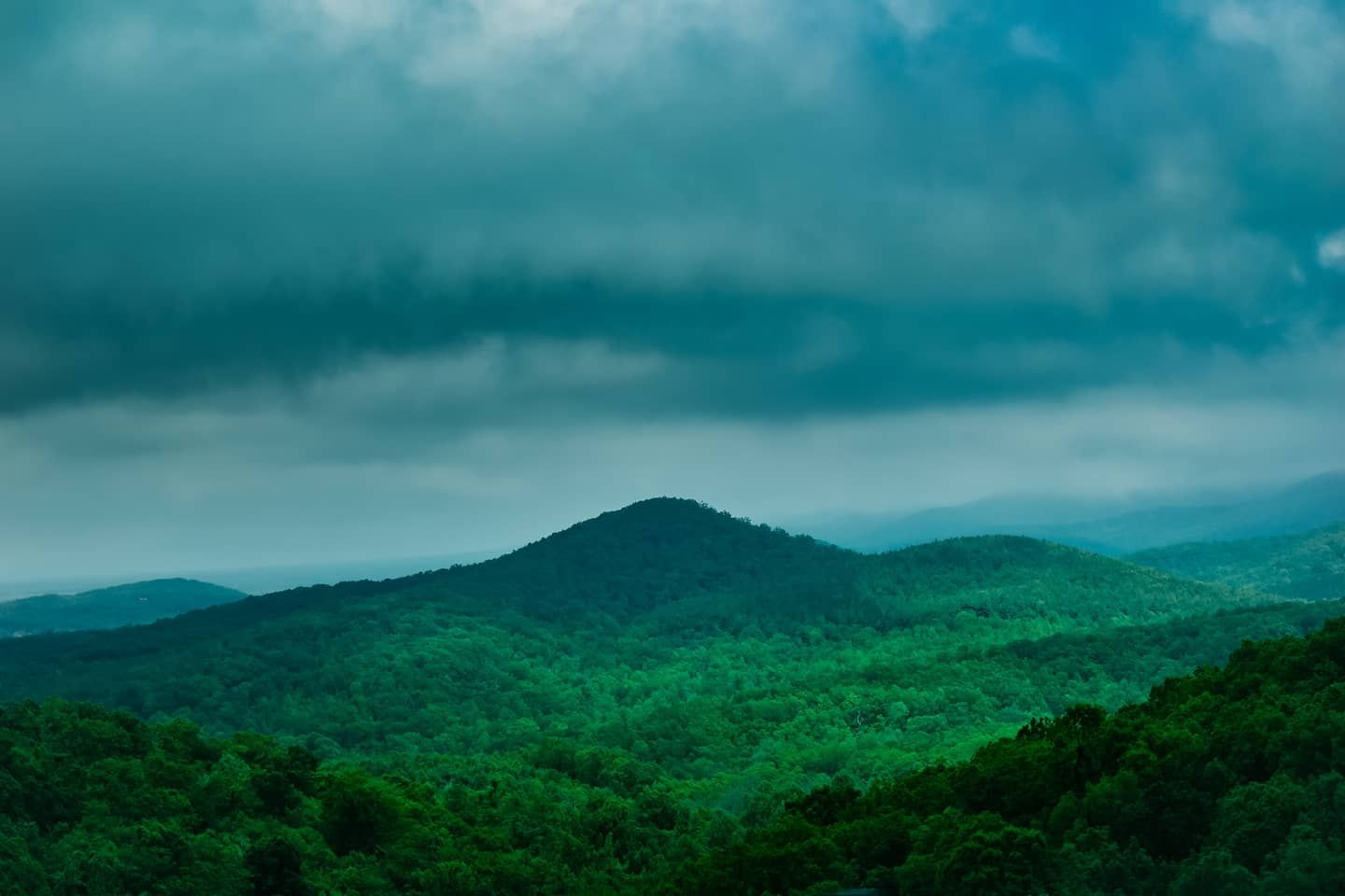 Rolling green mountains under dark stormy clouds create a moody landscape scene.