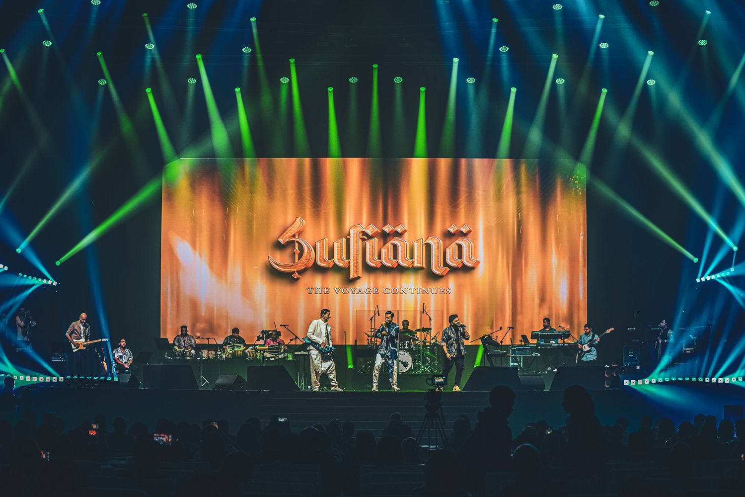 Concert stage illuminated with dramatic blue and green lighting effects during a live performance.