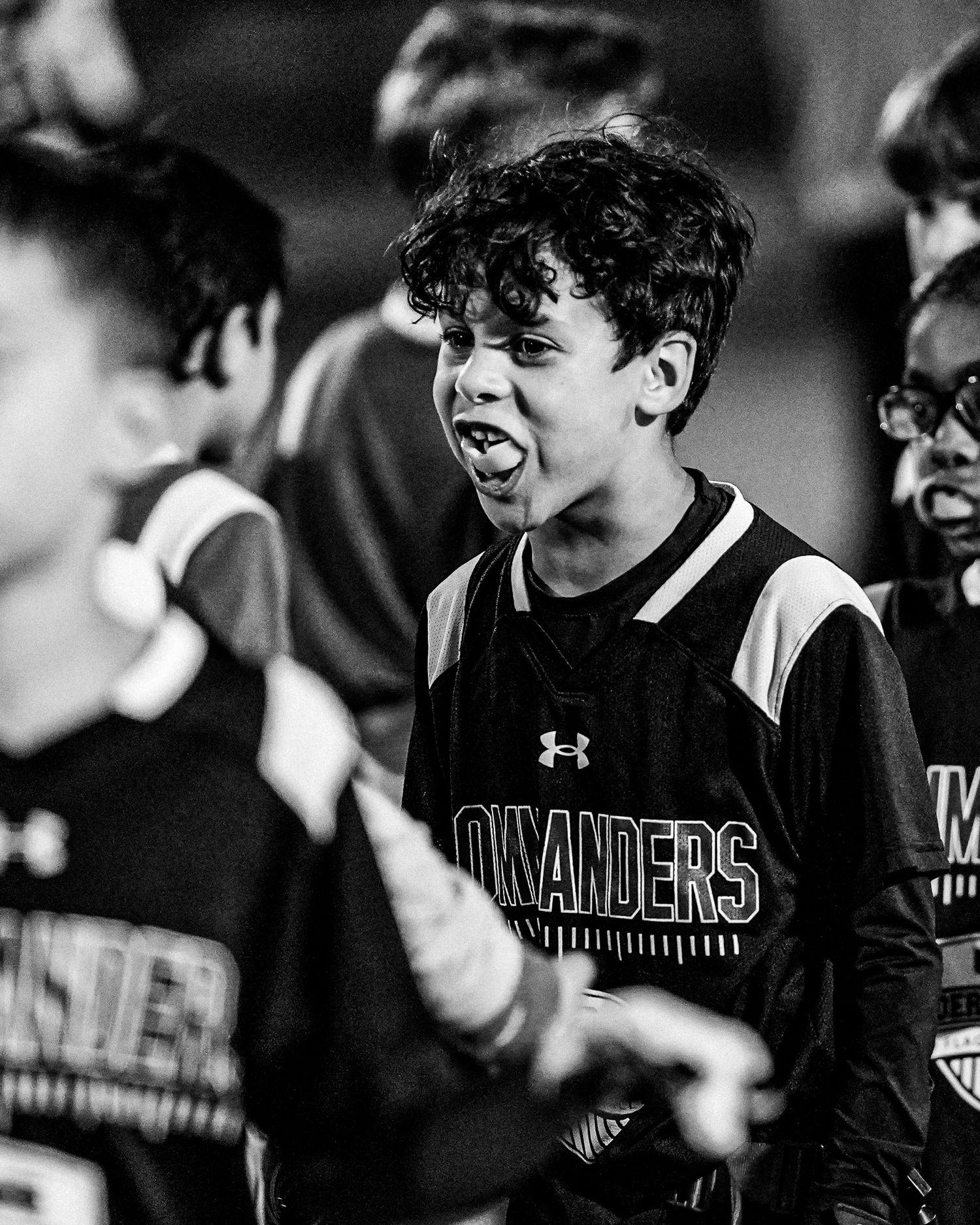 High school baseball players in black Under Armour uniforms celebrate together in a black and white photo.