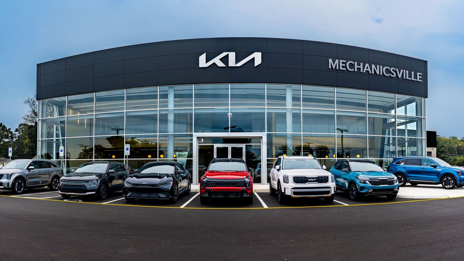 Modern Kia car dealership storefront in Mechanicsville with new vehicles displayed in front of glass facade building.