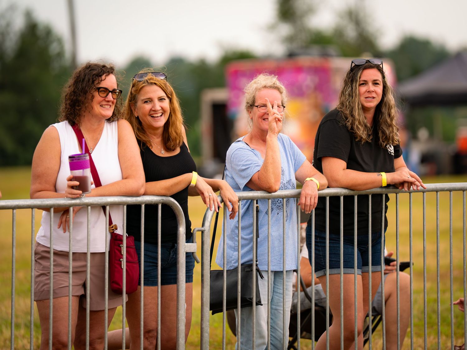 Spectators lean against a metal railing watching an outdoor event on a sunny summer day.