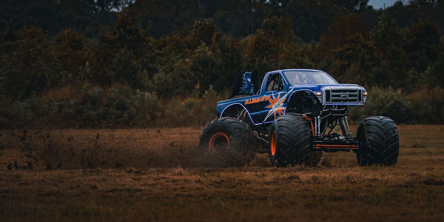 Row of monster trucks lined up on a dirt field during a performance.