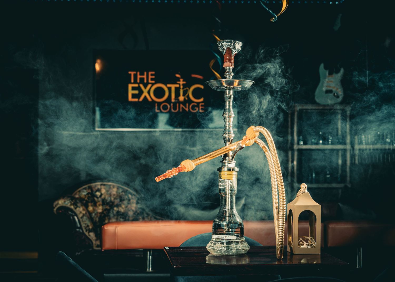 A luxurious hookah setup with an ornate glass pipe, lantern, and 'The Exotic' sign glowing in a moody dark setting.