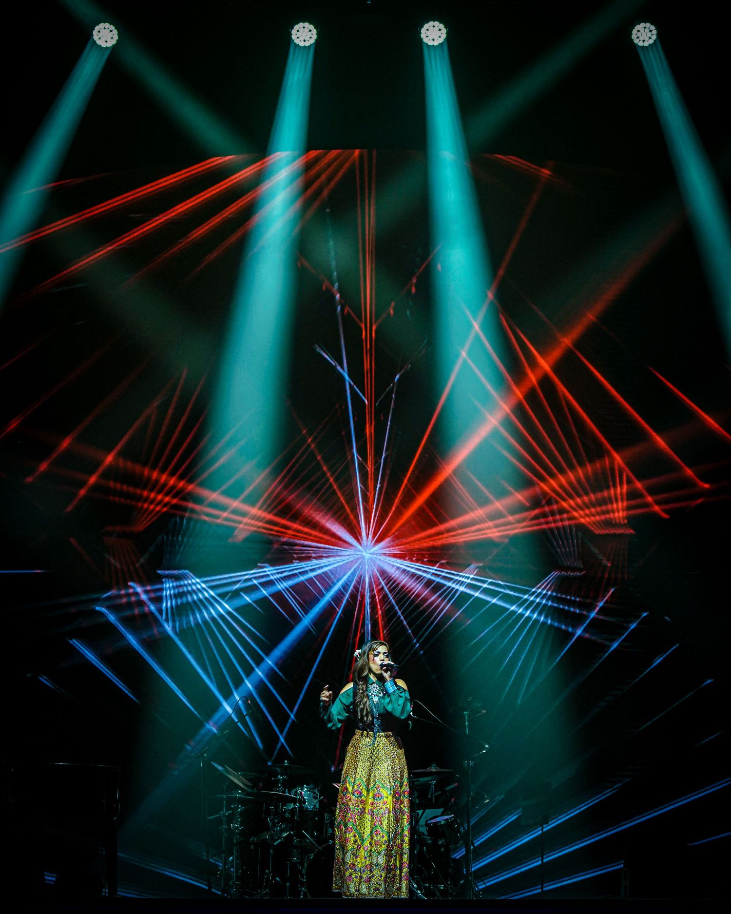 Dramatic concert lighting display with intersecting blue and red laser beams creating geometric patterns on dark stage.