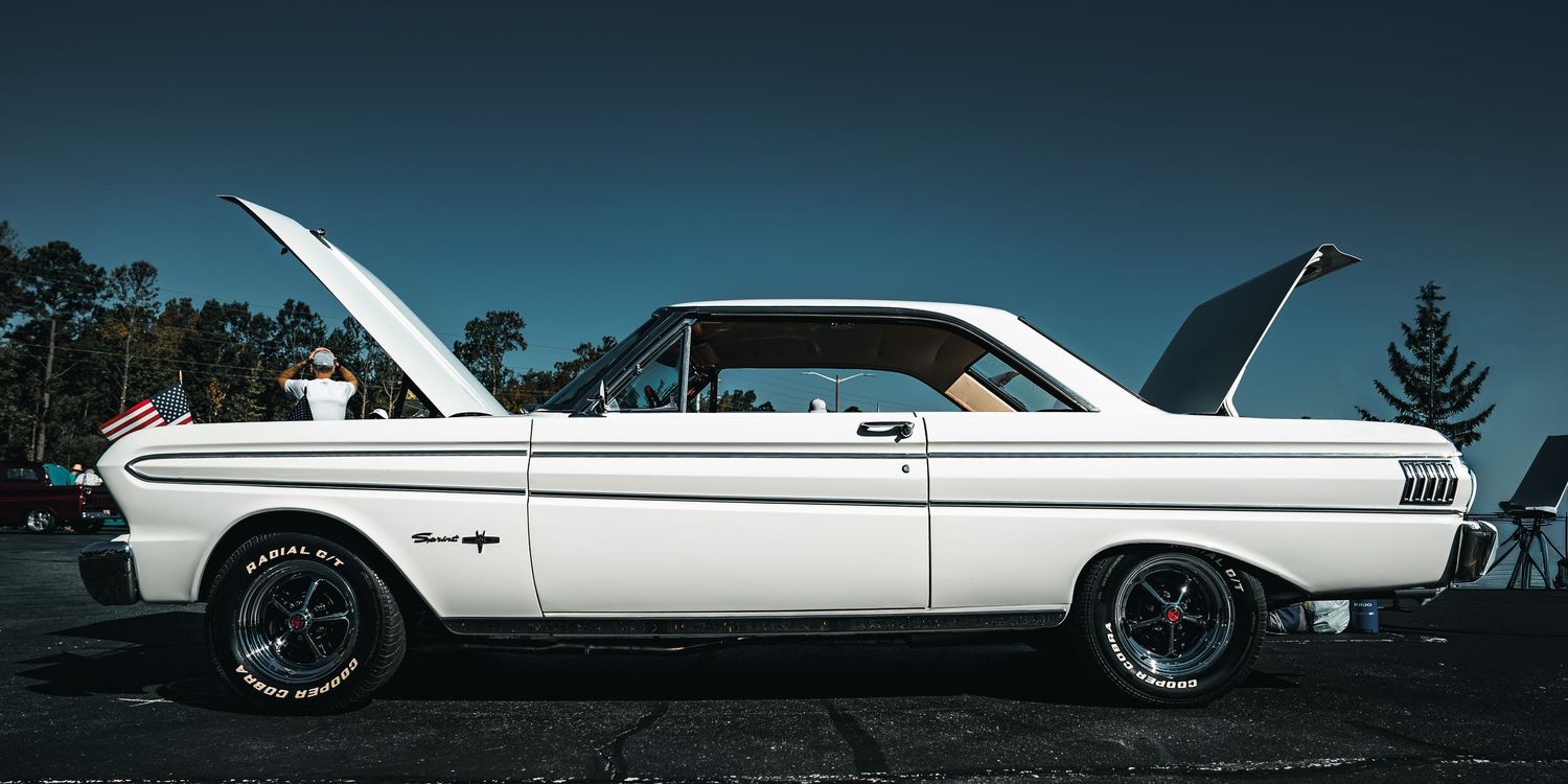 Classic white Ford Falcon hardtop coupe with custom wheels parked against dark background at dusk.