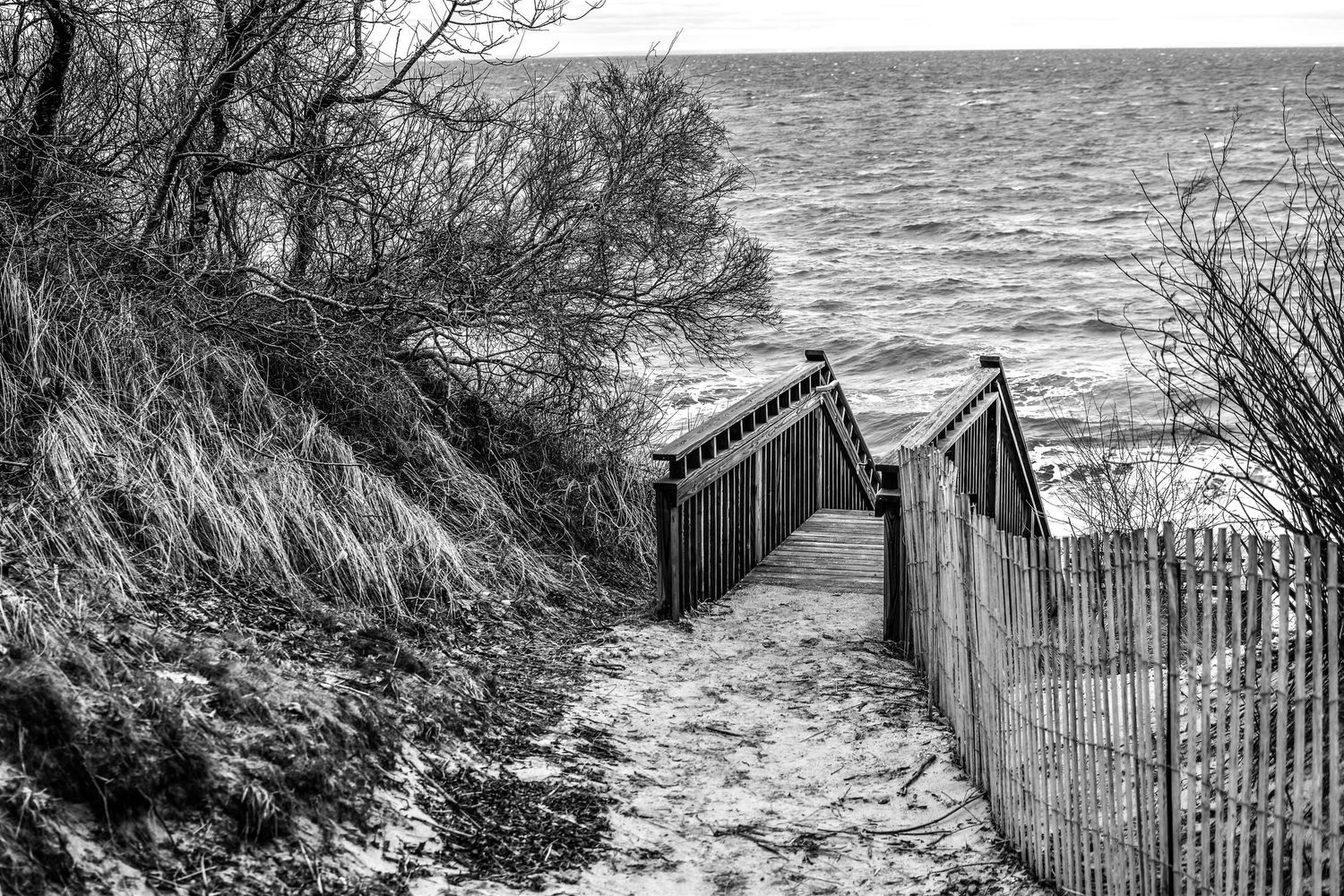 Rustic wooden fences line a coastal path overlooking a choppy gray ocean.