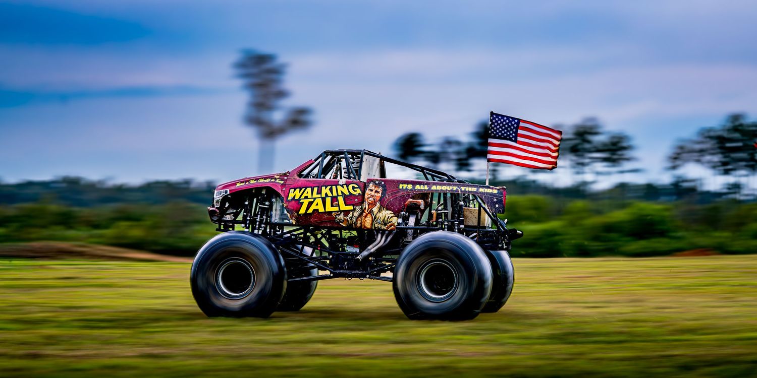 Monster trucks racing across field with American flags waving in motion blur.