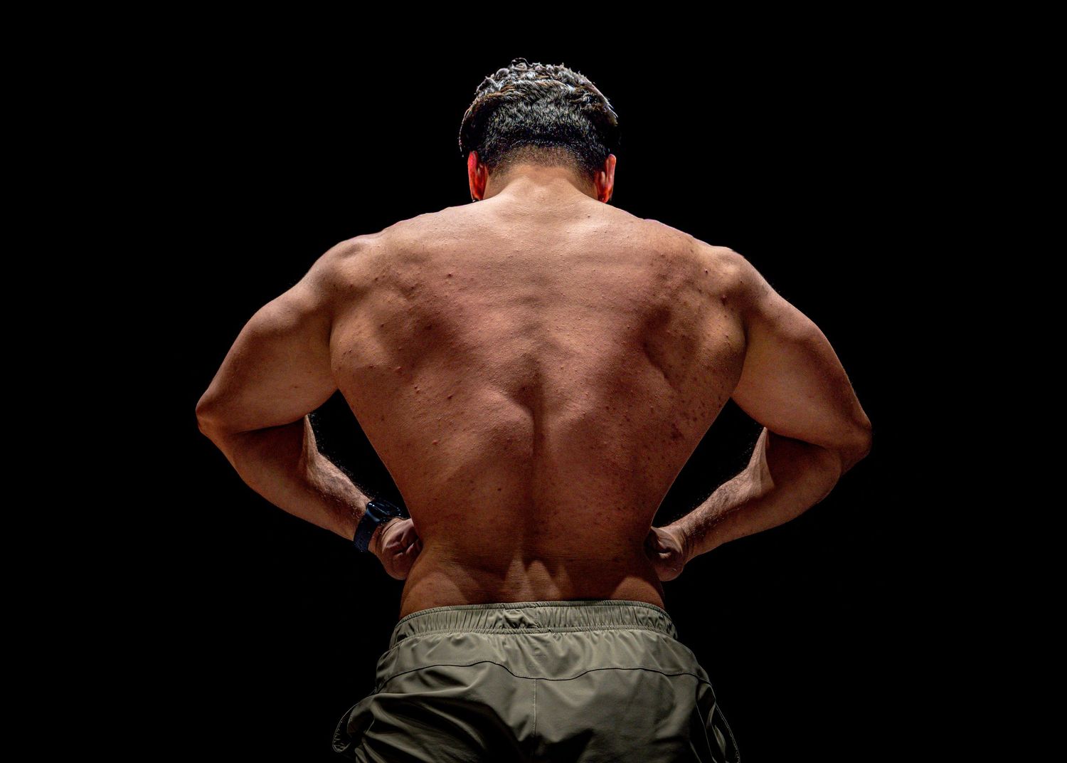Muscular shirtless man showing back muscles in dramatic lighting against dark background.