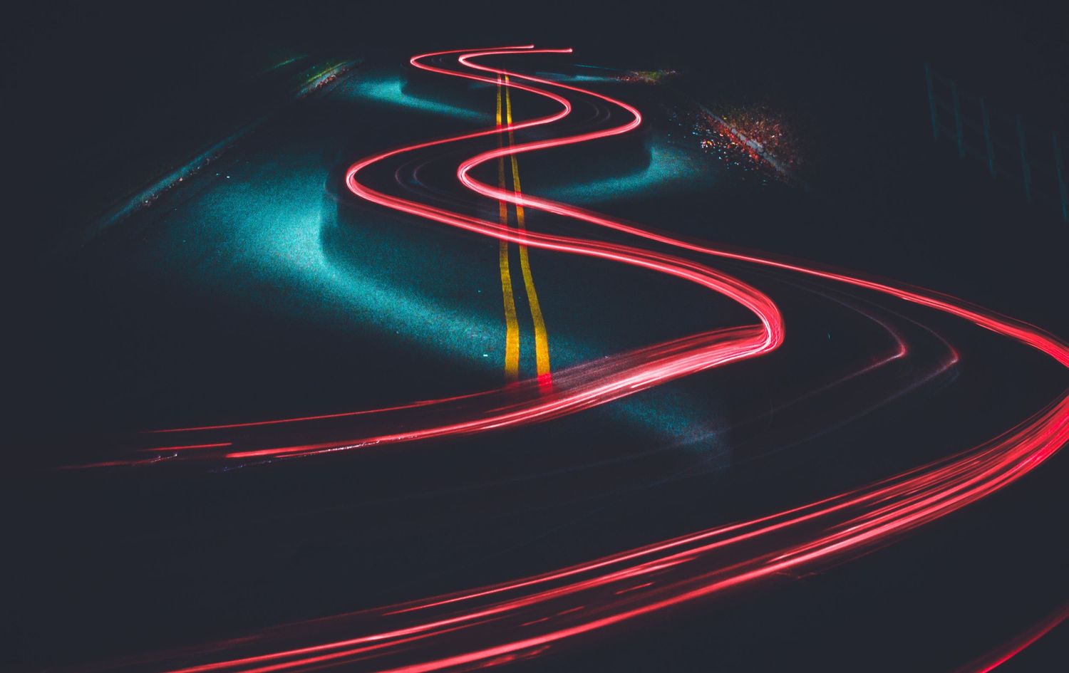 Long exposure photograph of winding red light trails against a dark background.