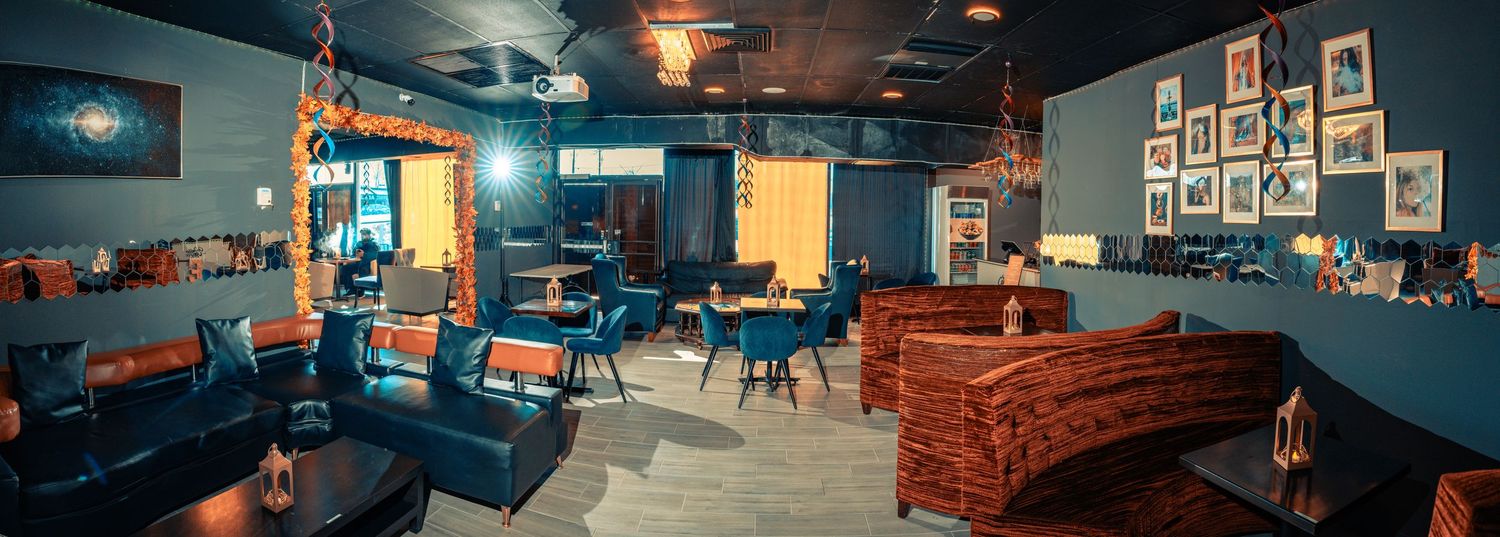 Panoramic view of a cozy lounge area with blue walls, leather couches and framed artwork in dim lighting.