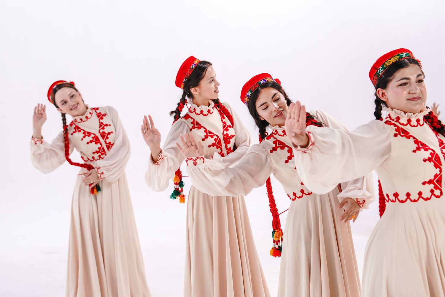 Four dancers in traditional white and red folk costumes with matching headdresses perform a synchronized dance routine.