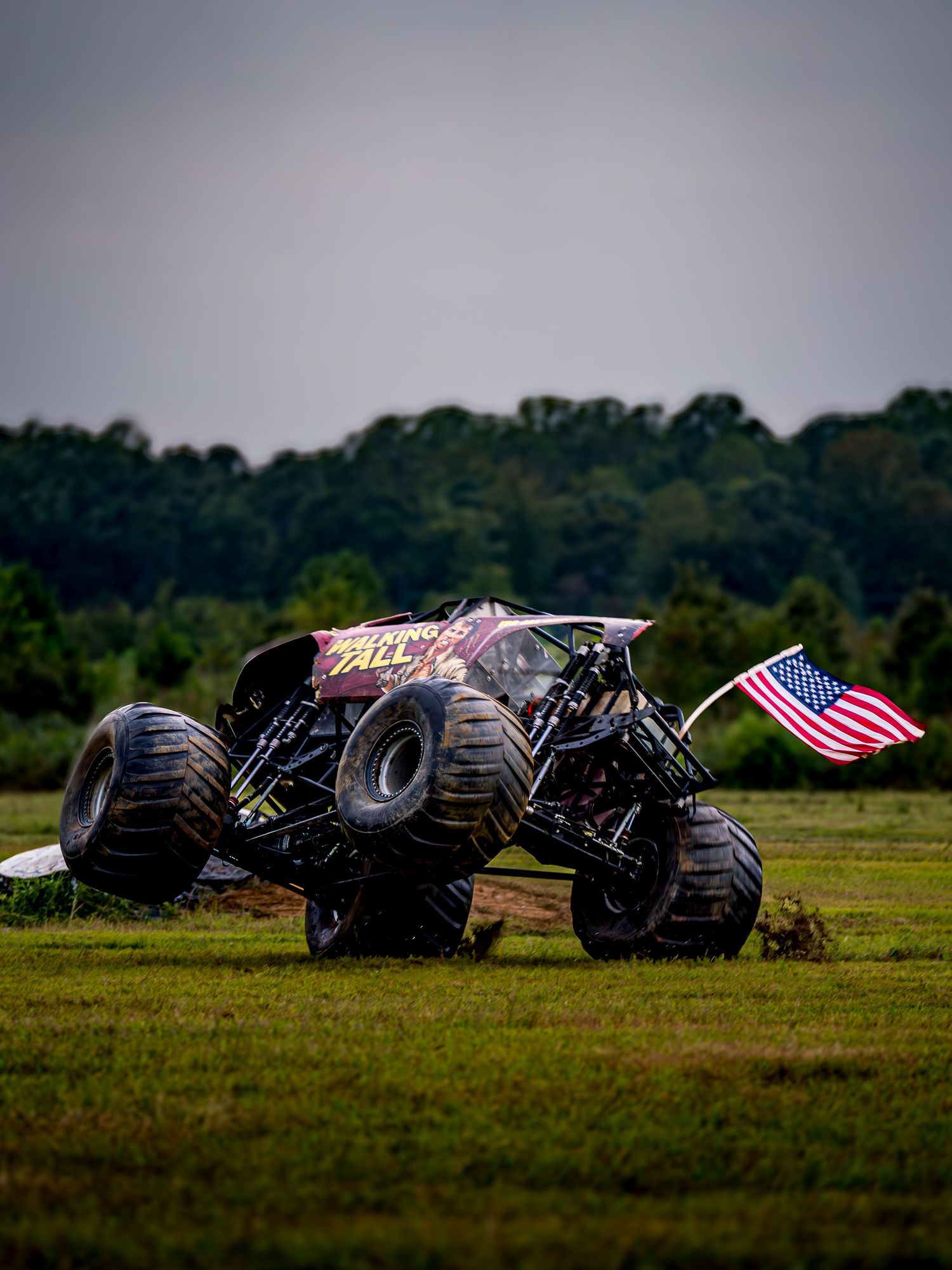 Monster trucks with American flags performing stunts in sequence on a grassy field.