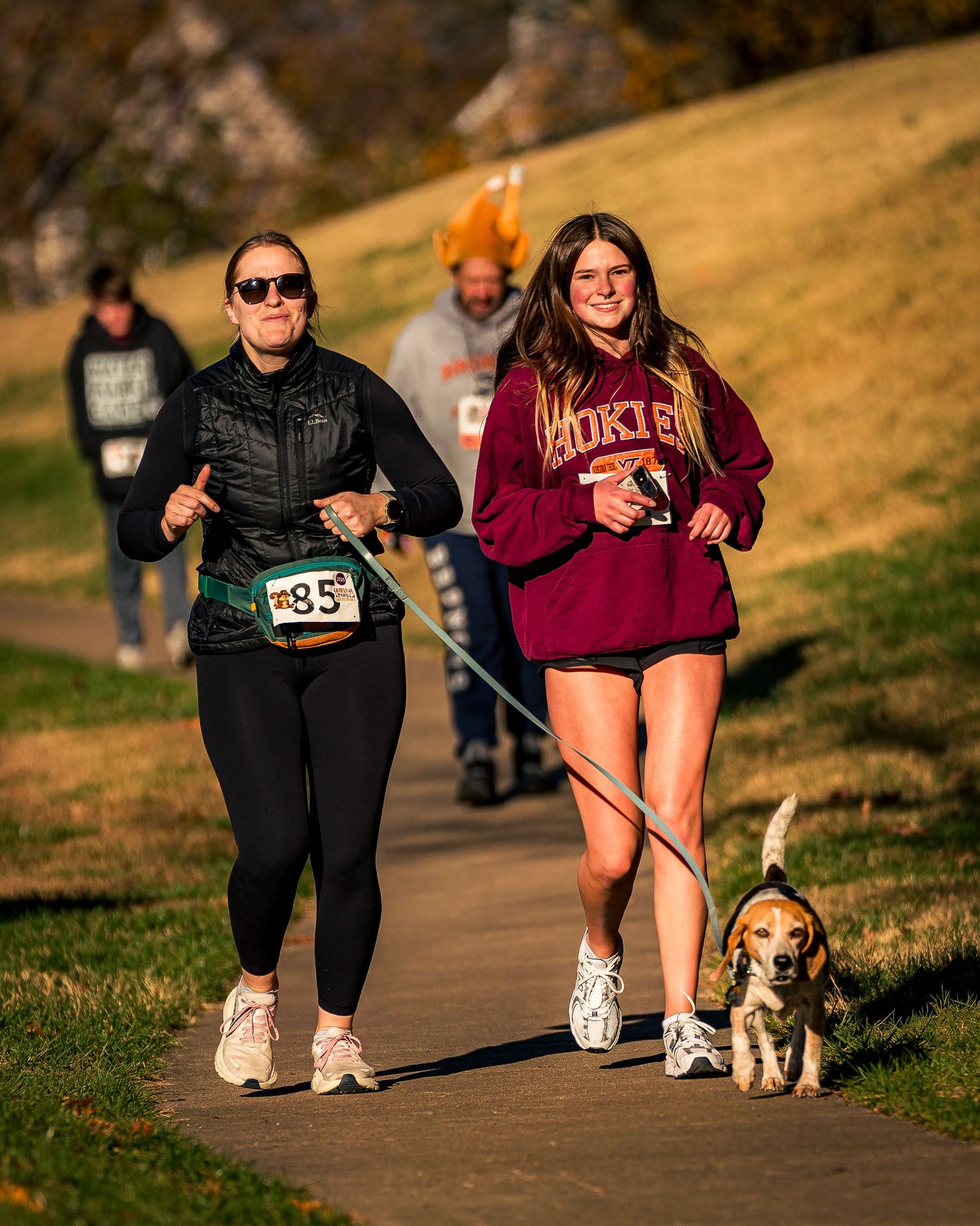 Runners and their dogs participating in a sunset race along a paved path.