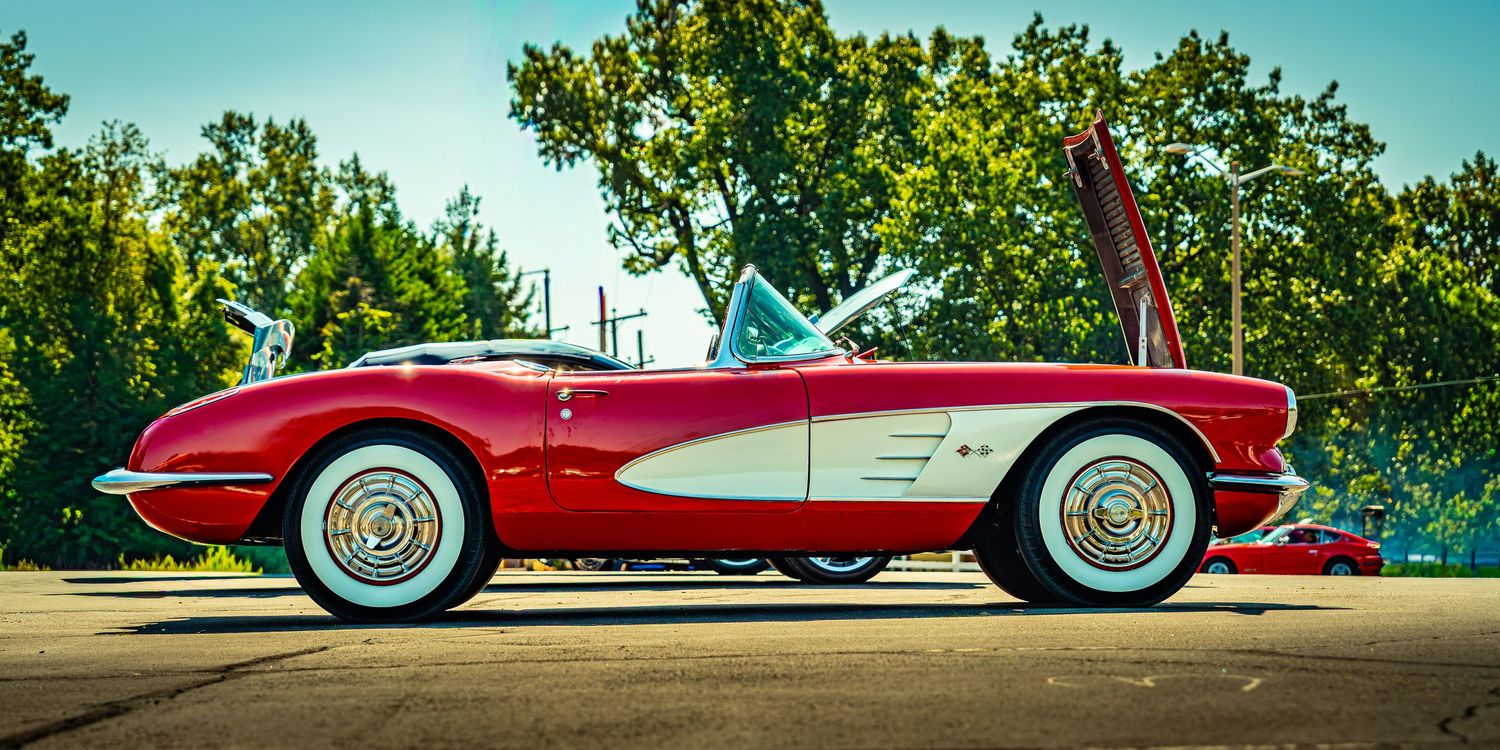 Classic red and white Chevrolet Corvette convertibles lined up at a vintage car show under blue sky.