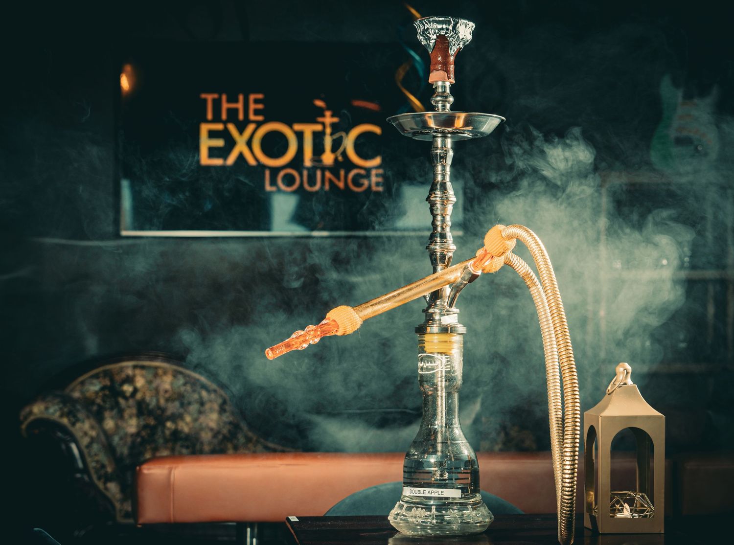 Elegant glass hookah pipe with smoke rising in a dimly lit exotic lounge atmosphere.