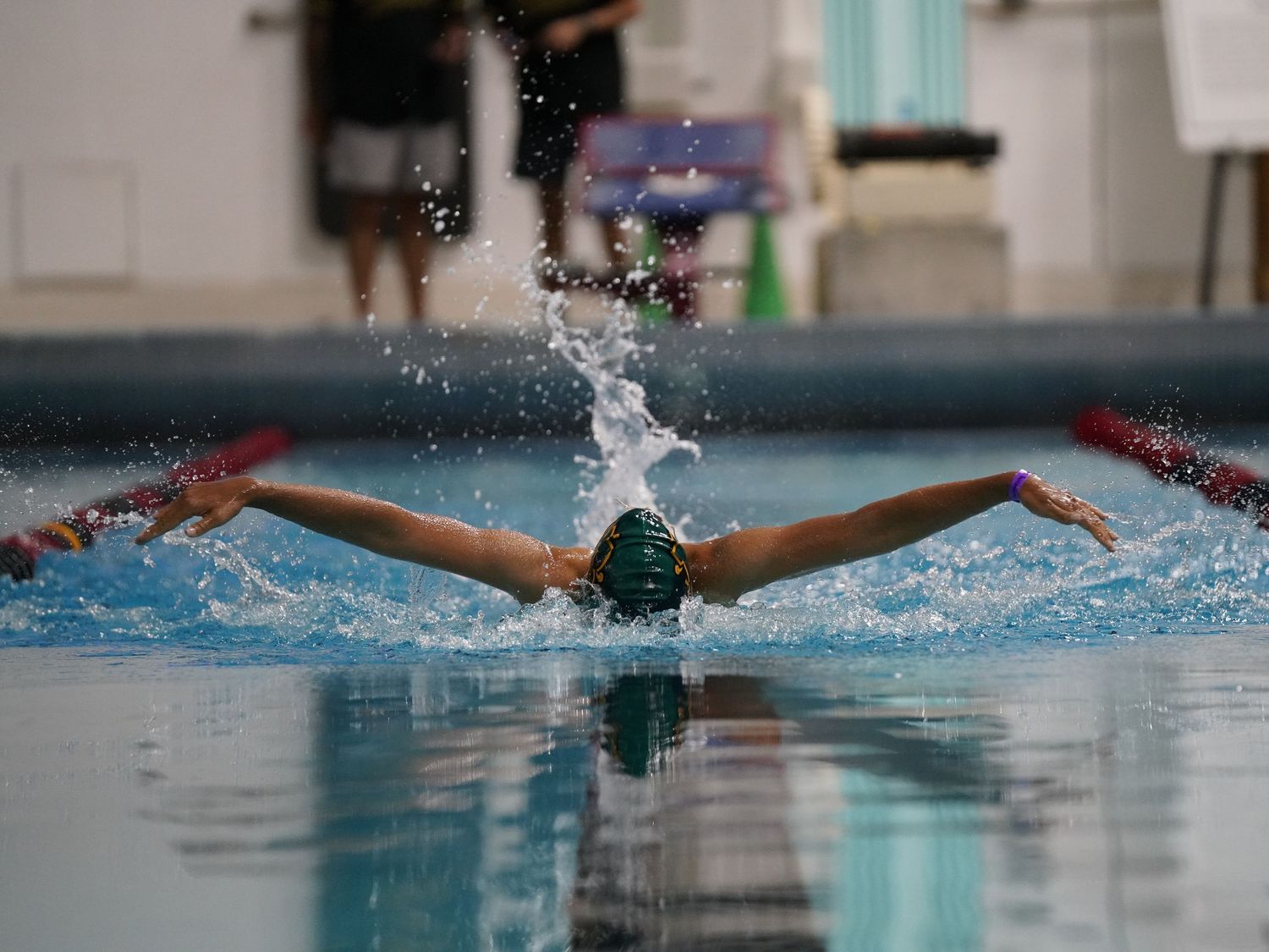 Swimmers performing butterfly stroke in an indoor pool during competition.