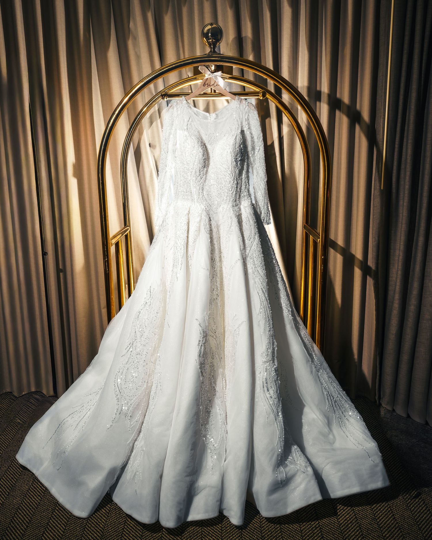 A white wedding dress illuminated from above showcases its voluminous skirt and intricate details in a dramatic display.