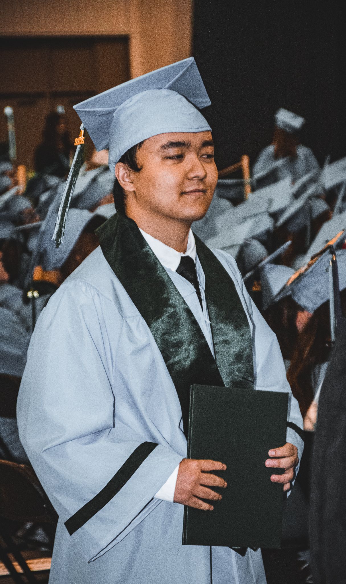 Graduate in light blue cap and gown holds diploma during graduation ceremony.