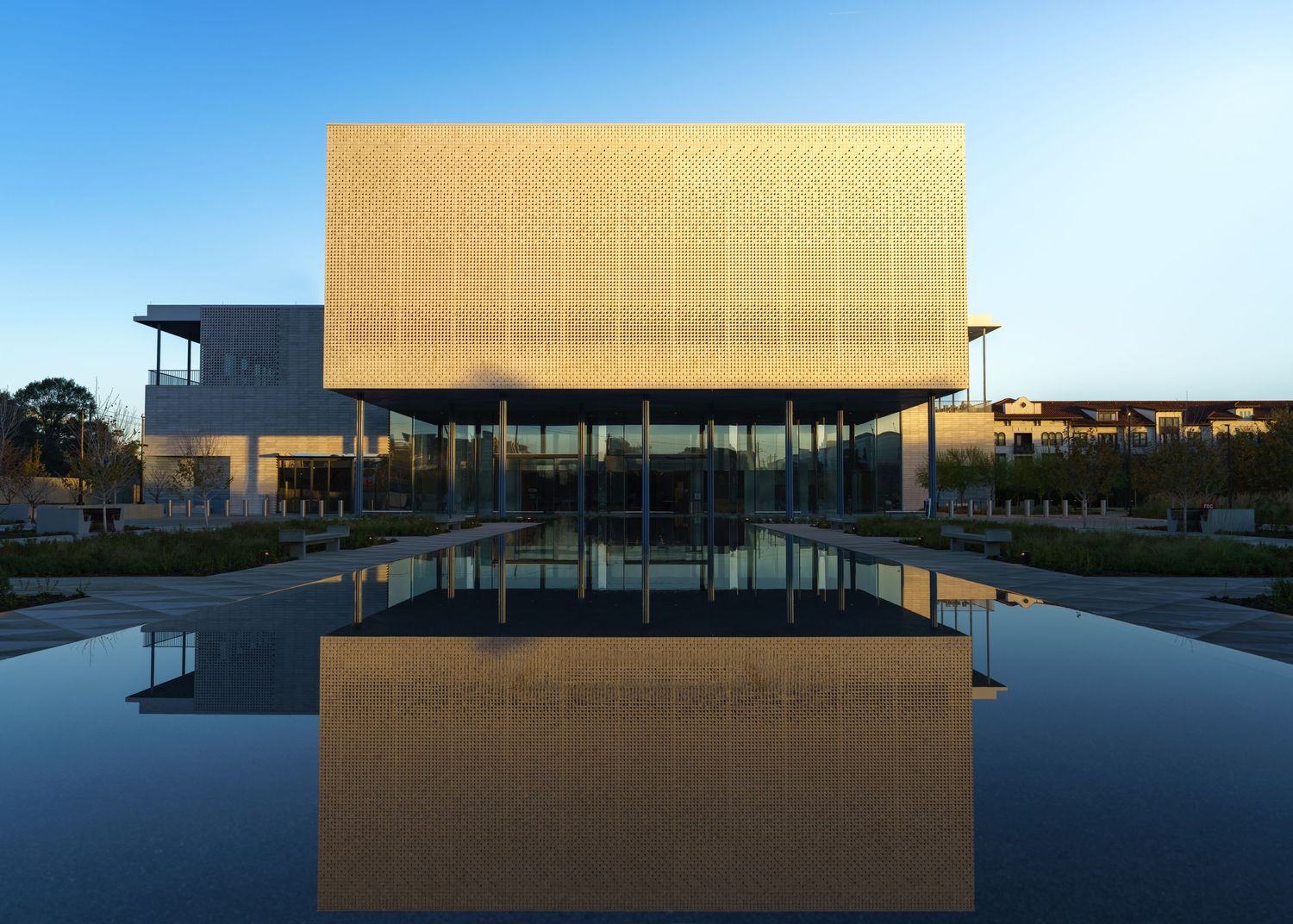 Panoramic view of a modern commercial building with glass facade reflecting golden sunlight at dusk. (The Ismaili Center Houston)