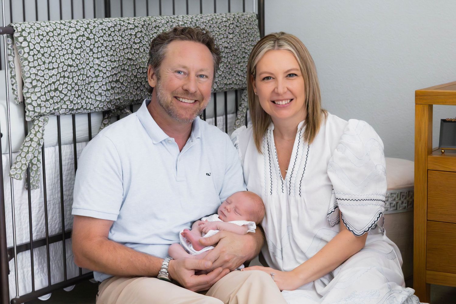 New parents hold baby and smile proudly at a newborn photo shoot