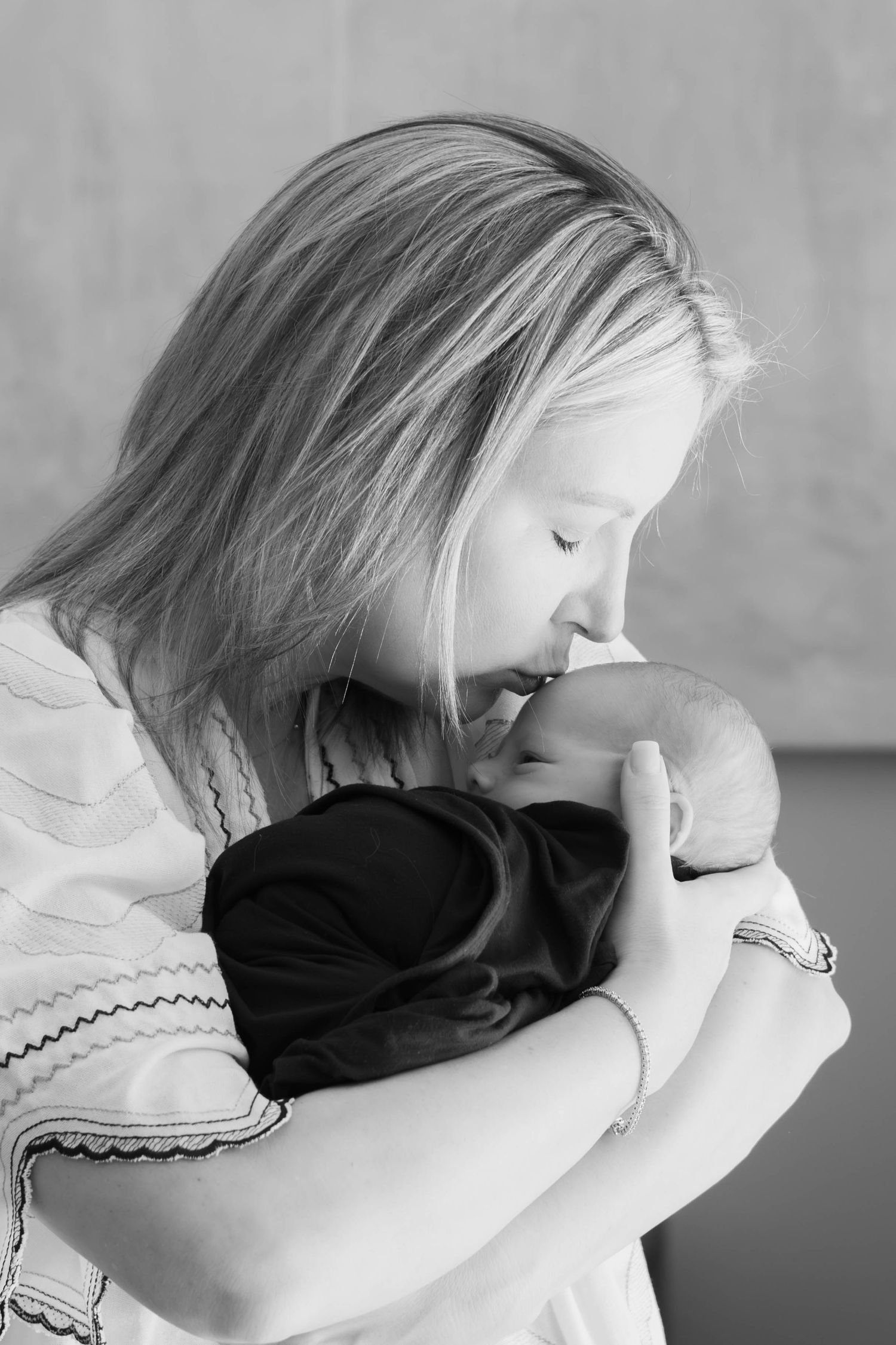 Sweet moment captured in natural light of new mom kissing baby boy