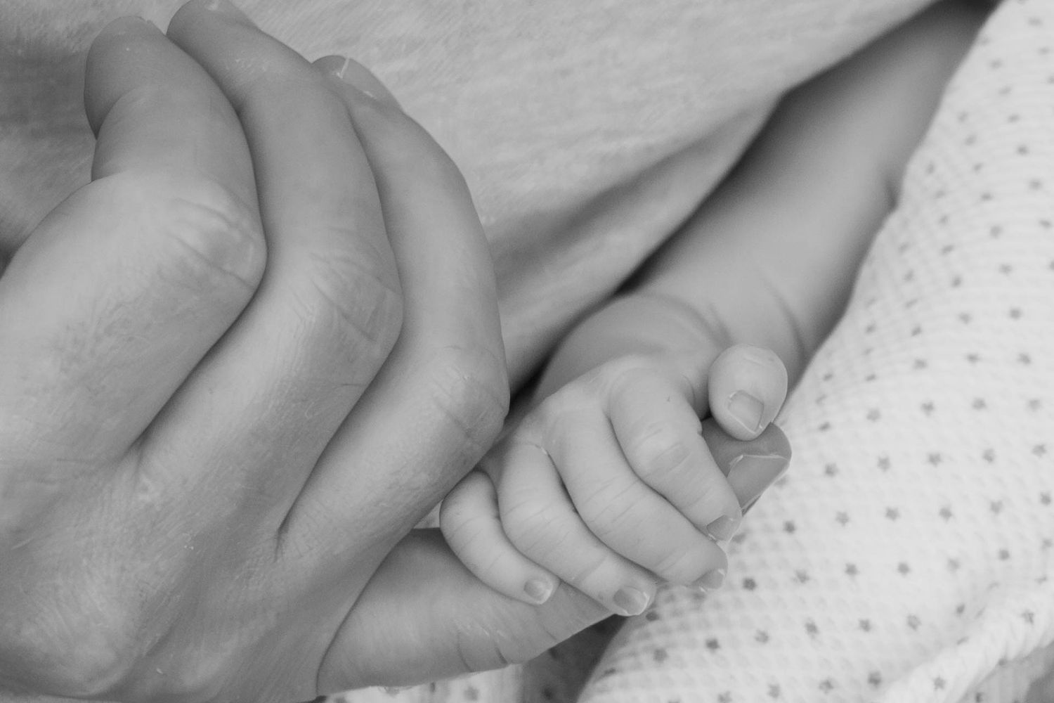 Tiny newborn hand wraps around dad's finger