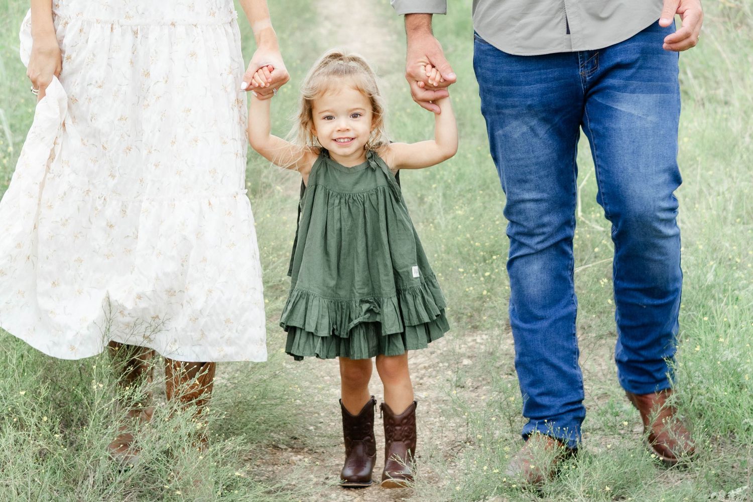 Toddler girl holds parents hands in a DFW family photo shoot