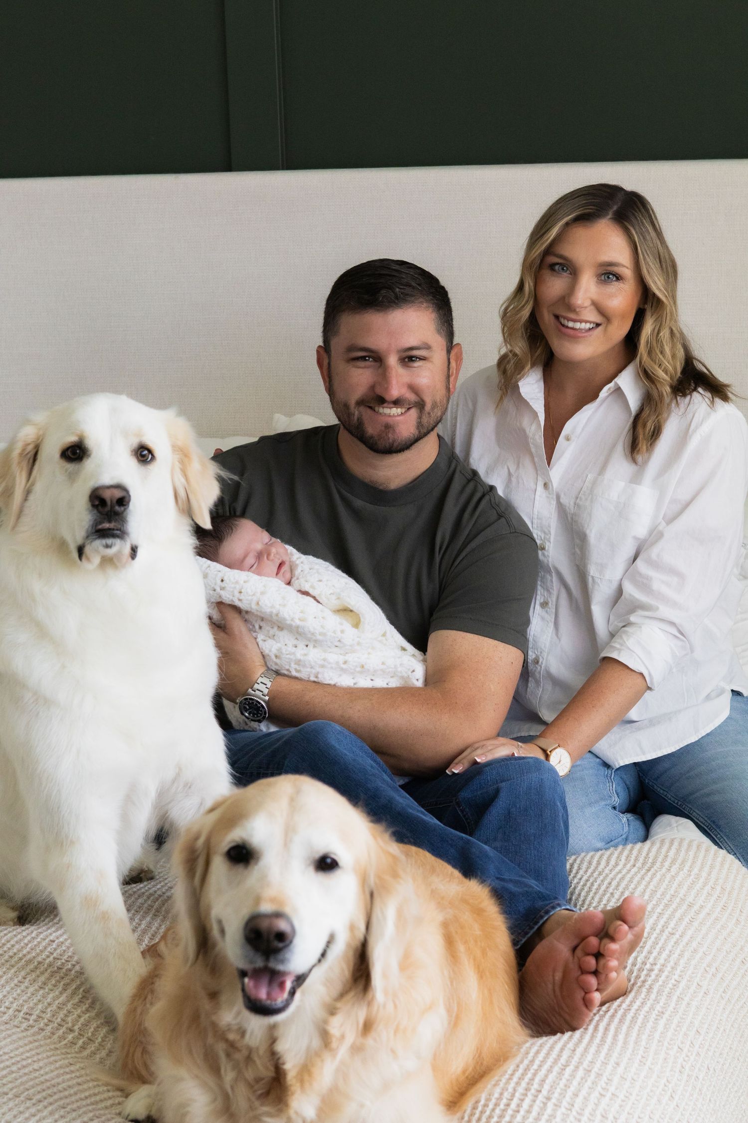 Family of 3 and 2 dogs all gather together on the bed and smile for the camera