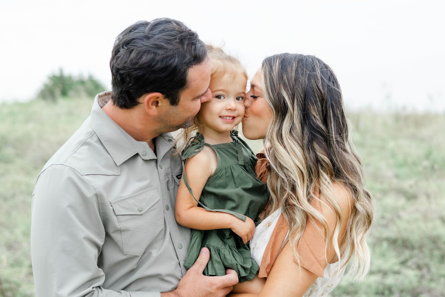 Dallas family of three gather together in a field during a family photo shoot